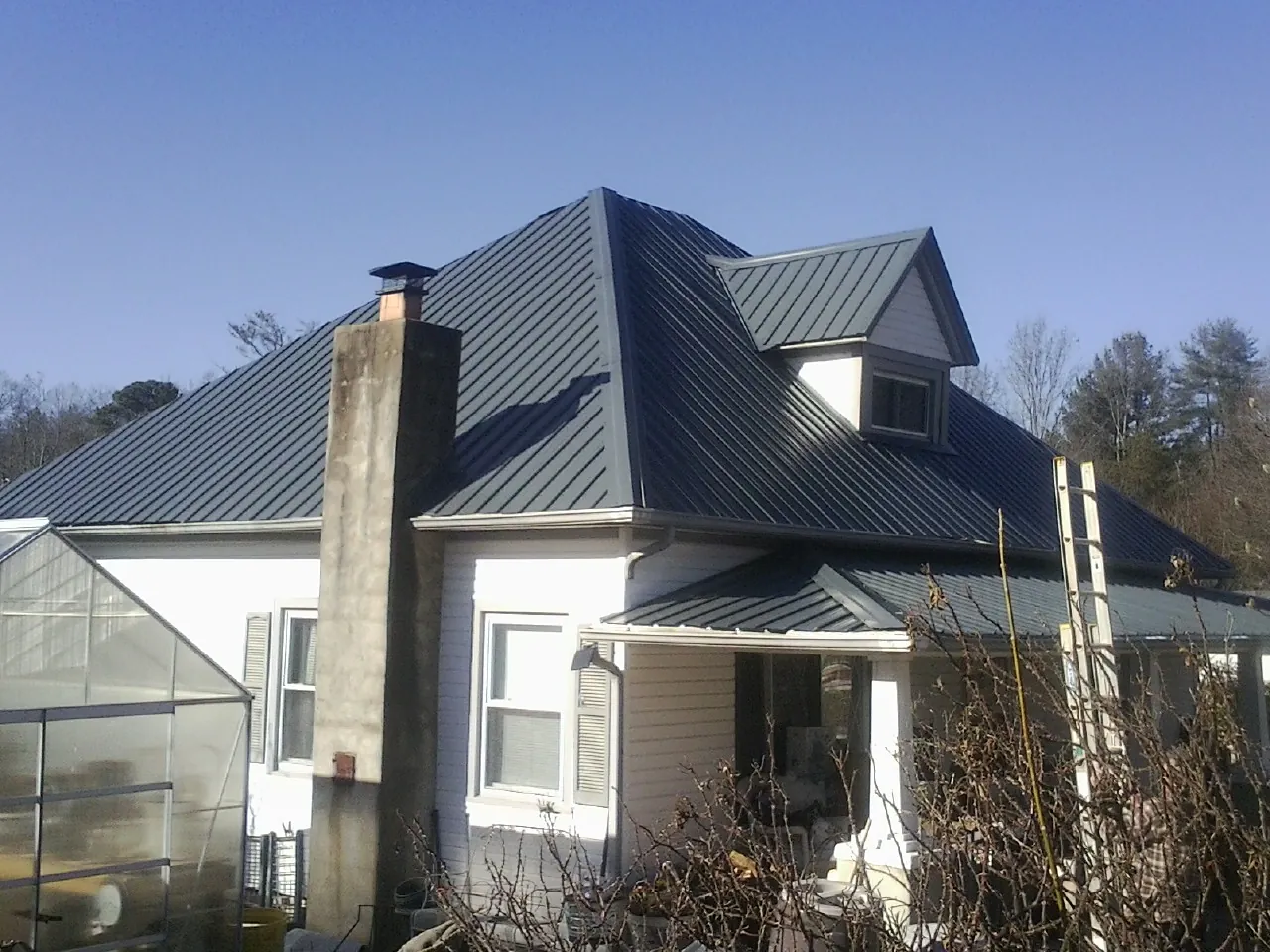 Dark blue standing seam metal roof on a white farmhouse with dormer — Slate & Tile Roof Repair by Roofing Brothers in Almond