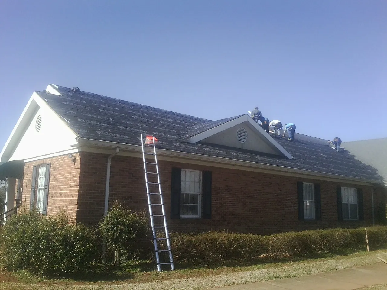 Crew tearing shingles off a brick ranch roof with a ladder set — Emergency Roof Repair work by our crew in Almond