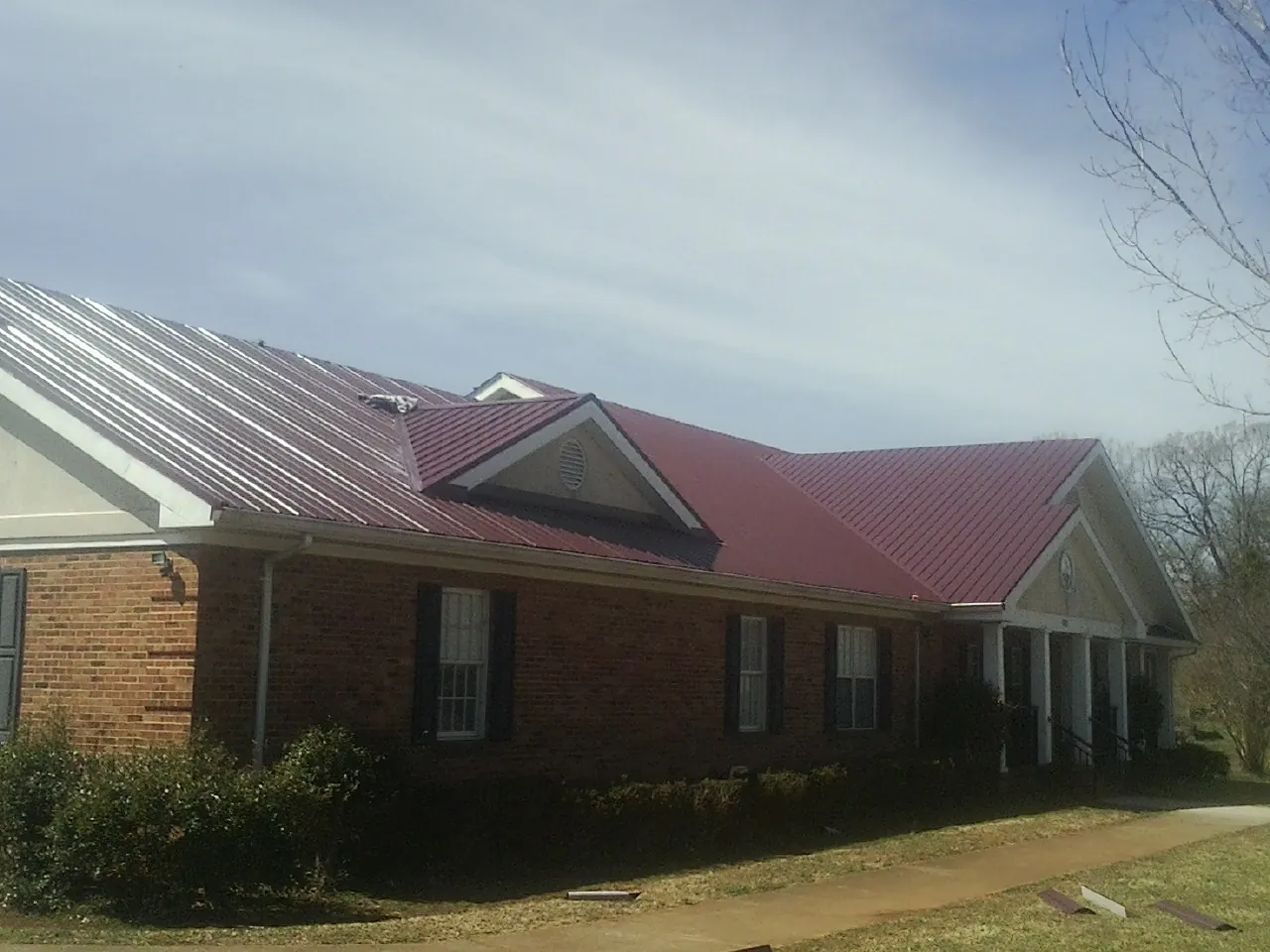 Red metal roof with gabled entries on a long brick building, from a Hail Damage Roof Repair job in Almond