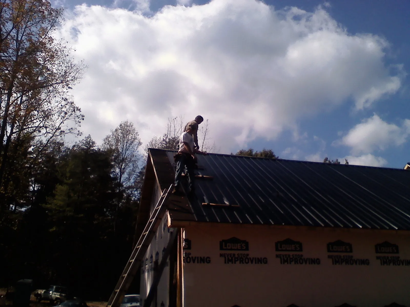 Roofer fastening dark metal panels high against a cloudy sky, from a Roof Inspection job in Almond