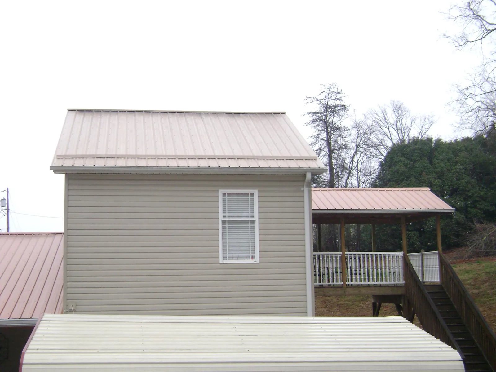 Tan metal roofs on a two story addition and attached porch, from a Roof Replacement job in Almond